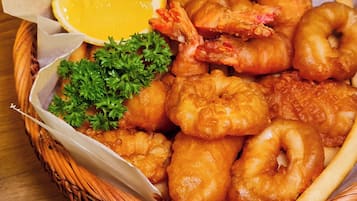 Un panier de fruits de mer frits, comprenant des crevettes, des coquilles Saint-Jacques et des rondelles de calamars, servi avec des quartiers de citron et du persil.