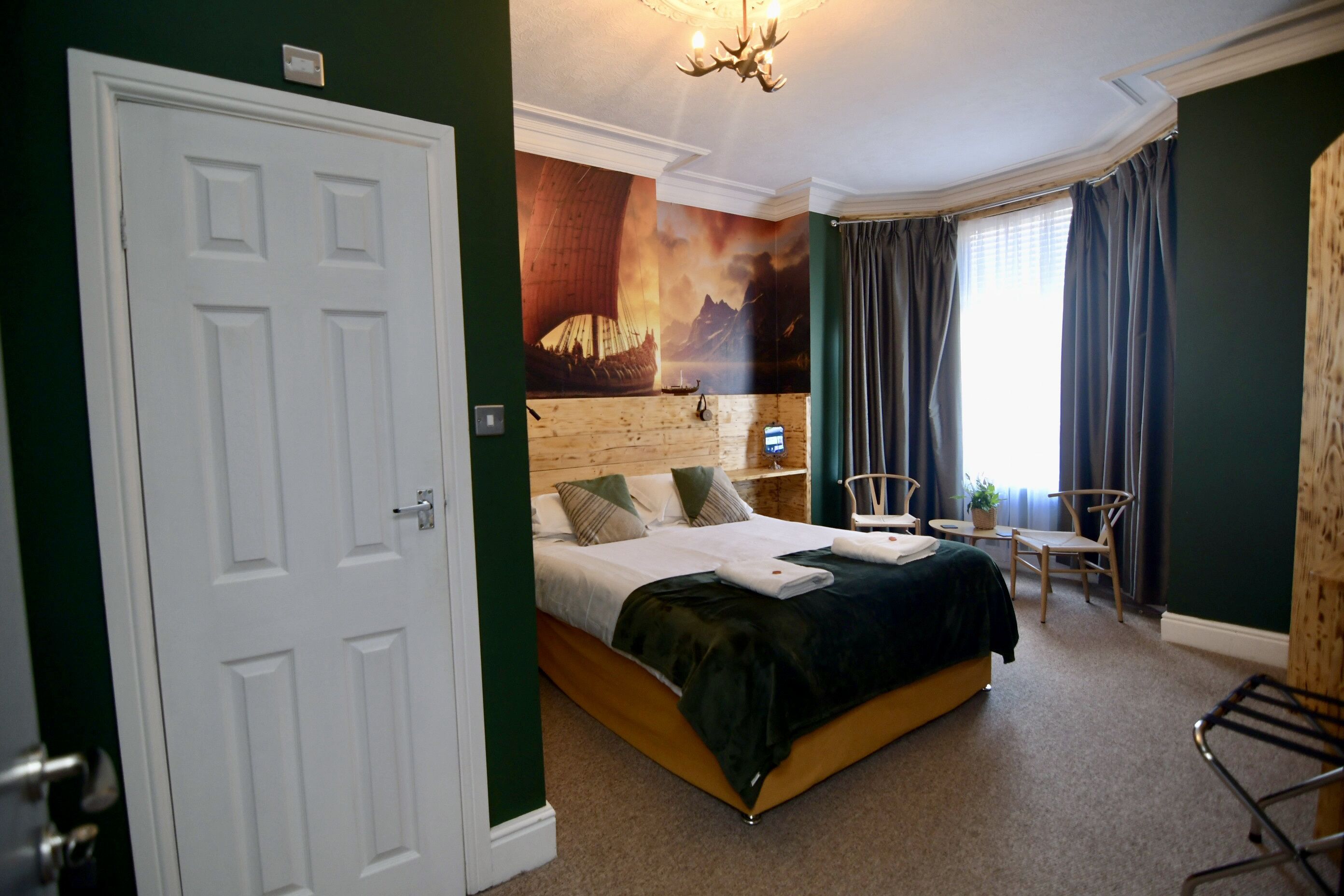 A hotel room with a bed, a desk, a chair, a window with curtains, and a wall mural.