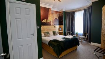 A hotel room with a bed, a desk, a chair, a window with curtains, and a wall mural.