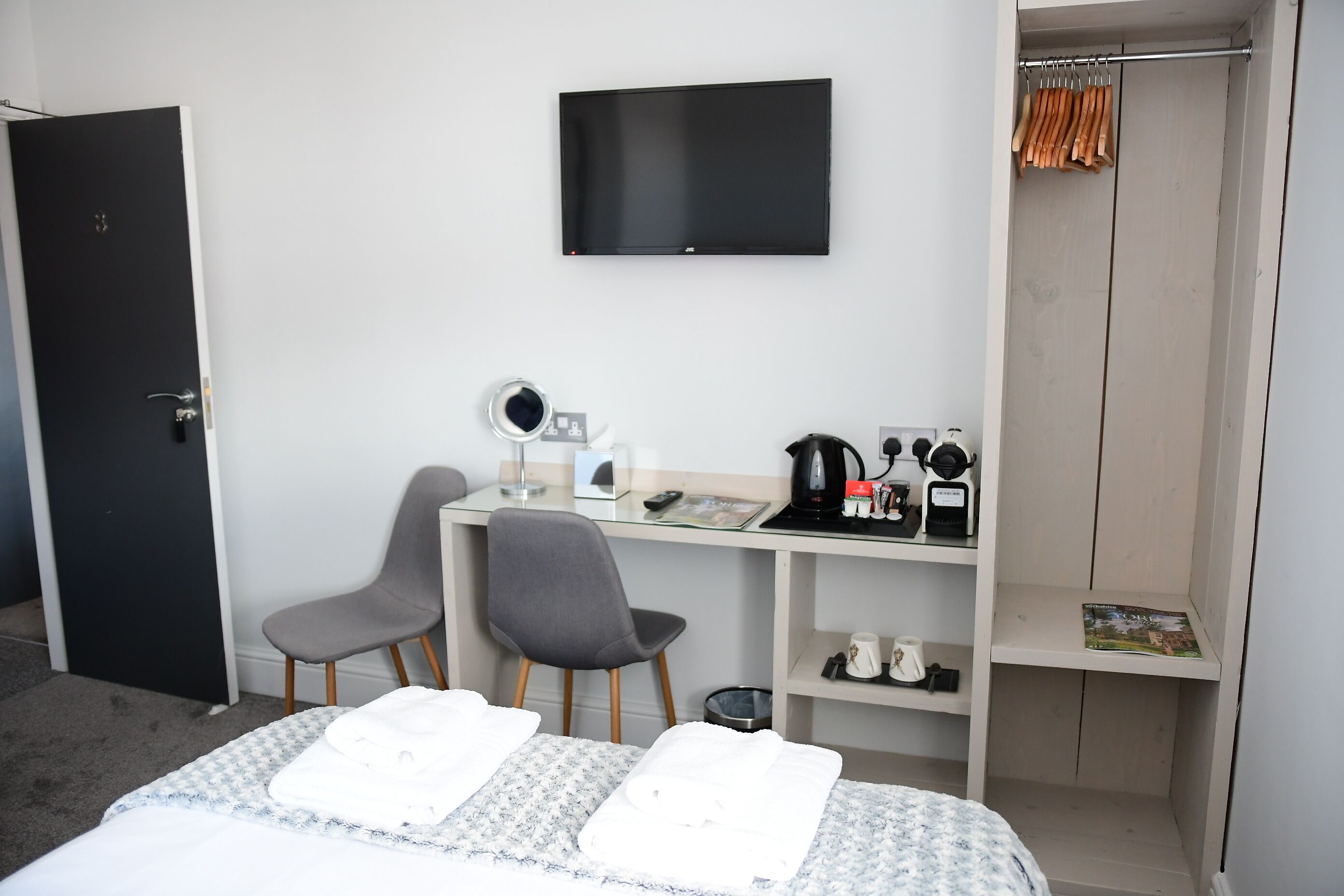 A hotel room with a bed, two chairs, a desk with a computer, a television, and a wardrobe.
