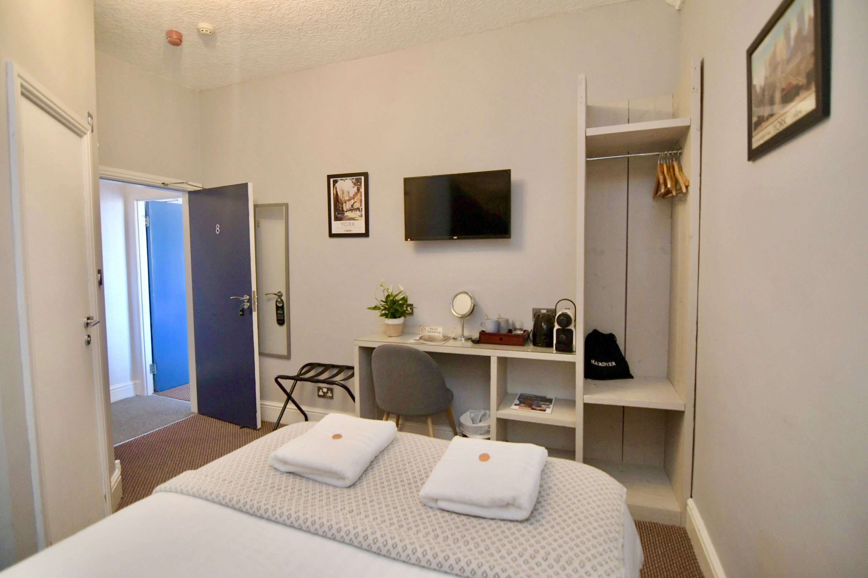 A hotel room with a bed, a desk, a TV, a closet, and a door leading to another room.