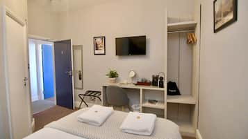 A hotel room with a bed, a desk, a TV, a closet, and a door leading to another room.