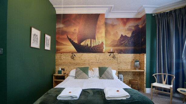 A hotel room with a large bed, wooden headboard, green walls, and a mural of a sailboat. - Vikings Accommodation (York)
