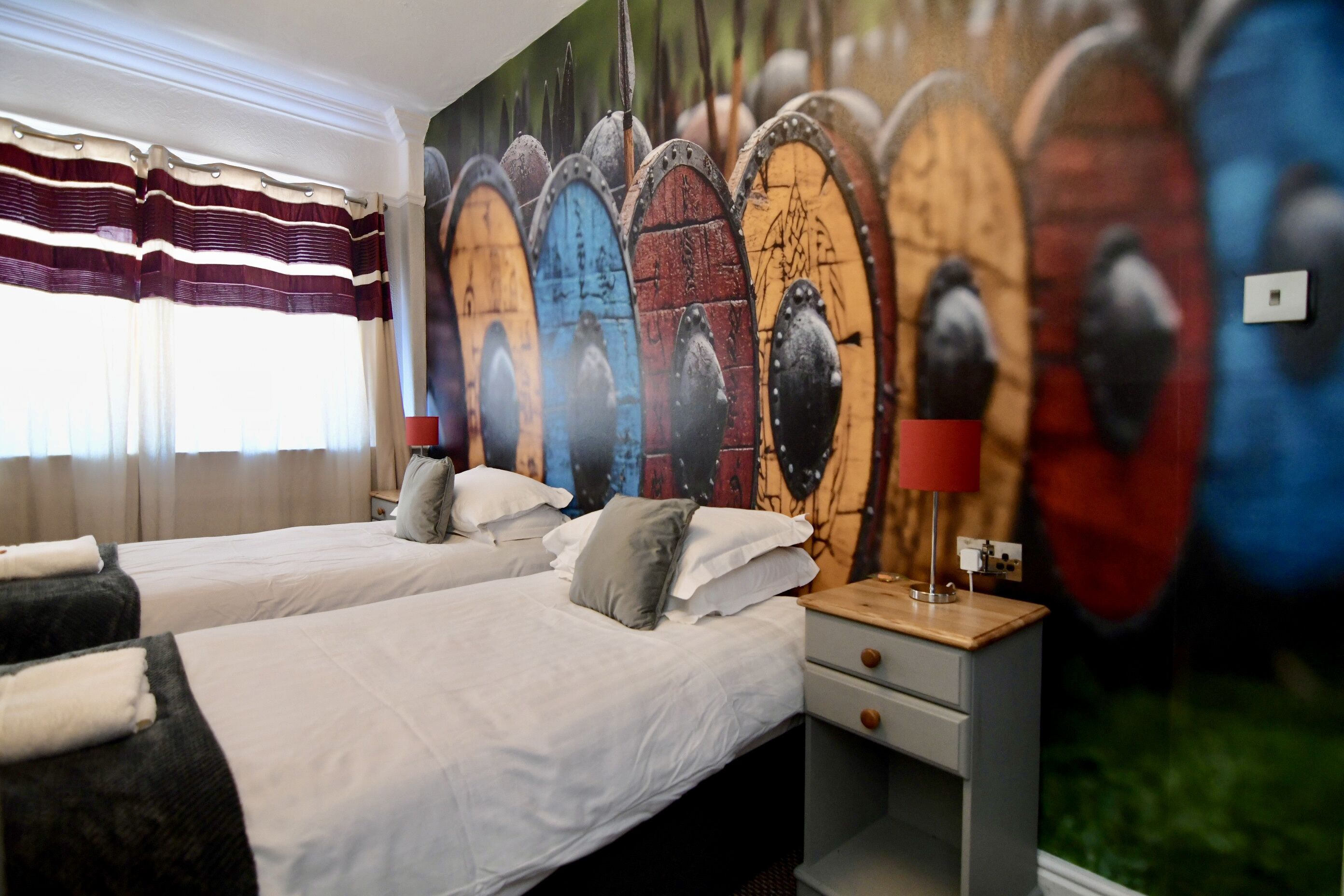 Habitación de hotel con dos camas, un mural grande y una ventana con cortinas.