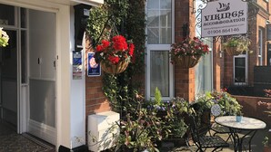 A brick building with a sign for 'Vikings Accommodation'. There are outdoor seating areas with tables and chairs, and hanging flower baskets. - Vikings Accommodation (York)