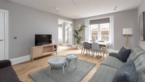 A modern living room with a sofa, a TV, a dining area, and a large window.