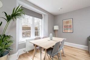 A dining area with a table, chairs, a radiator, a potted plant, and a window with a view.