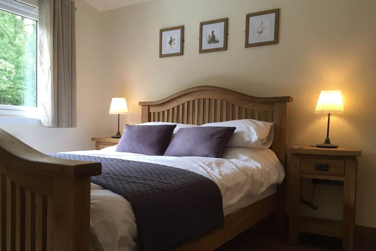 A neatly made bed with a wooden headboard, two bedside tables with lamps, and three framed pictures on the wall.