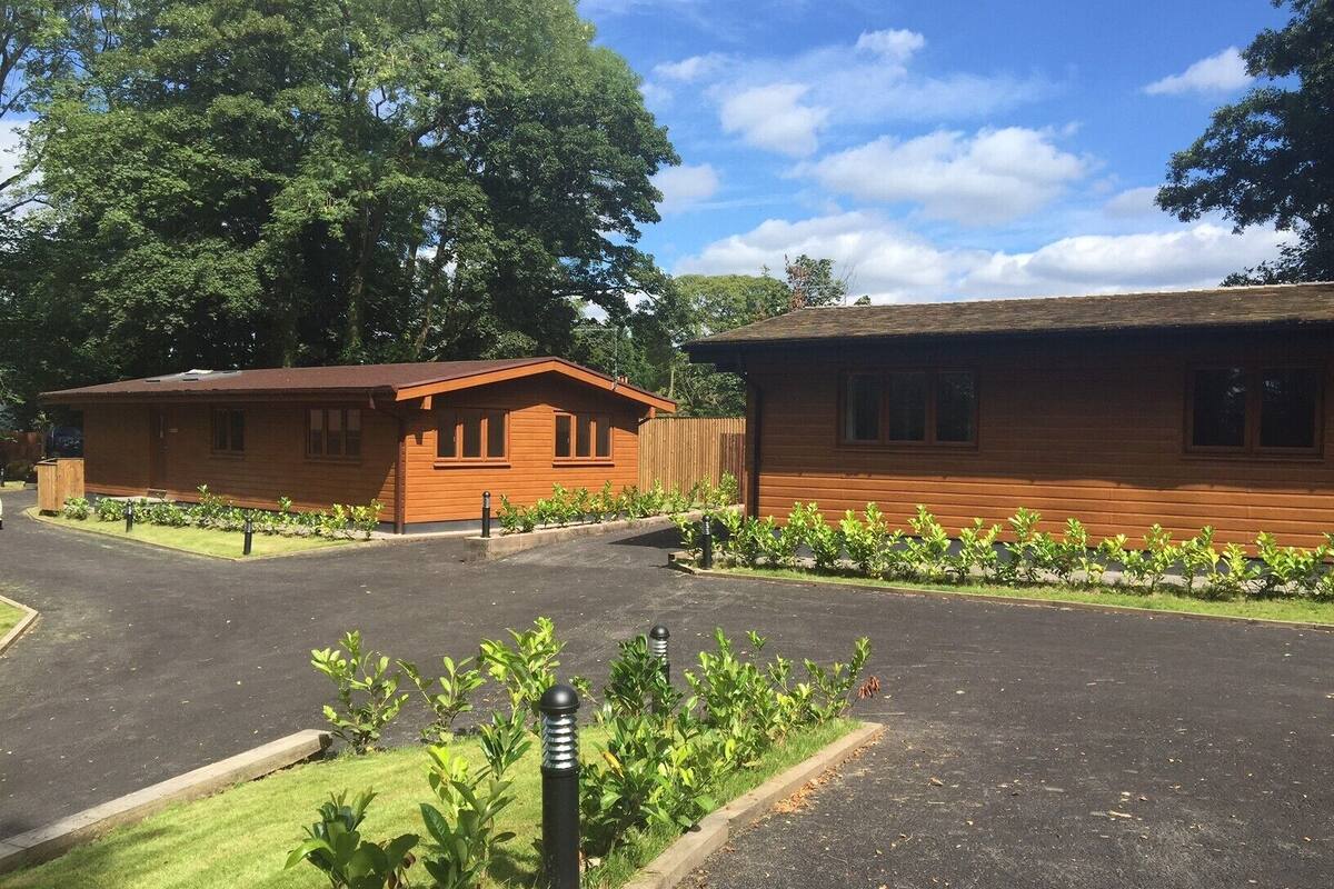 A wooden cabin-style building with a sloped roof, surrounded by a well-maintained lawn and small shrubs.