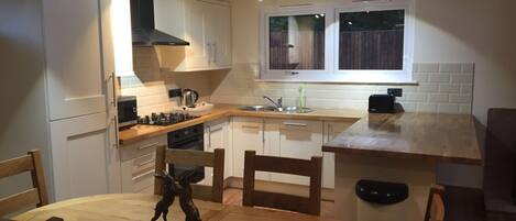 A compact kitchen with white cabinets, a wooden countertop, a gas stove, and a dining area with a round table and chairs.