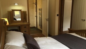 Un dormitorio con cama, cómoda con espejo, zona de ducha y puerta que da a otra habitación.