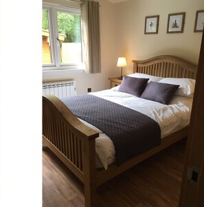 A wooden bed with a headboard, a bedside table with a lamp, and a window with curtains.