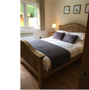 A wooden bed with a headboard, a bedside table with a lamp, and a window with curtains.