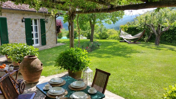A stone house with green shutters, a table set with plates and cups, and a hammock in the garden. - Villa with pool and garden (Città di Castello)