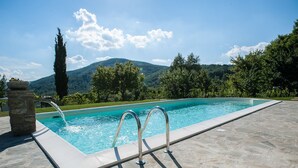A swimming pool with a stone structure on one side, surrounded by a stone deck and lush greenery. - Villa with pool and garden (Città di Castello)