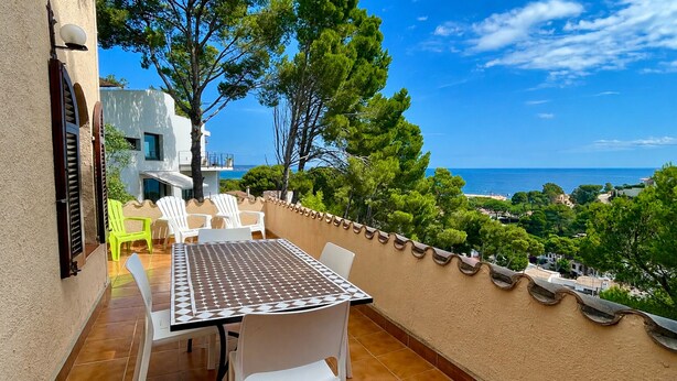 Une terrasse avec une table et des chaises, offrant une vue sur la côte, avec des arbres et des bâtiments.