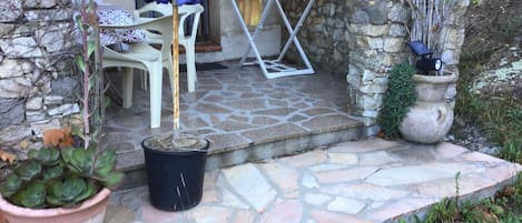 Een terras met stenen bestrating, buitenmeubilair, een bloempot en een tafel met een blauwe parasol.