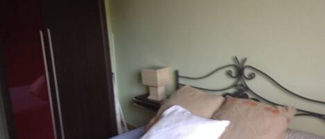 Ein Schlafzimmer mit einem Bett, Kissen, einem Nachttisch mit Lampe und einem Kleiderschrank.