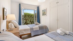 Un dormitorio con dos camas, una mesita de noche, una lámpara, un armario y una ventana con cortinas.