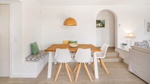 Un comedor con mesa de madera, sillas blancas, una lámpara colgante de fibras trenzadas y un banco con cojines.