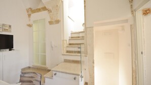A spacious room with a staircase leading to an upper floor, a flat-screen TV on a white cabinet, and a glass door. - Scirocco Apartment with Terrace by Wonderful Italy (Ostuni)