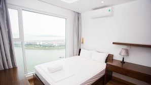 Une chambre d’hôtel avec un grand lit, une table de chevet en bois, un bureau et une vue sur le paysage urbain par une grande fenêtre.