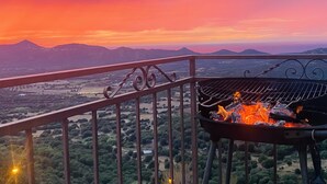 Un balcón con una parrilla y una vista panorámica de montañas al atardecer.