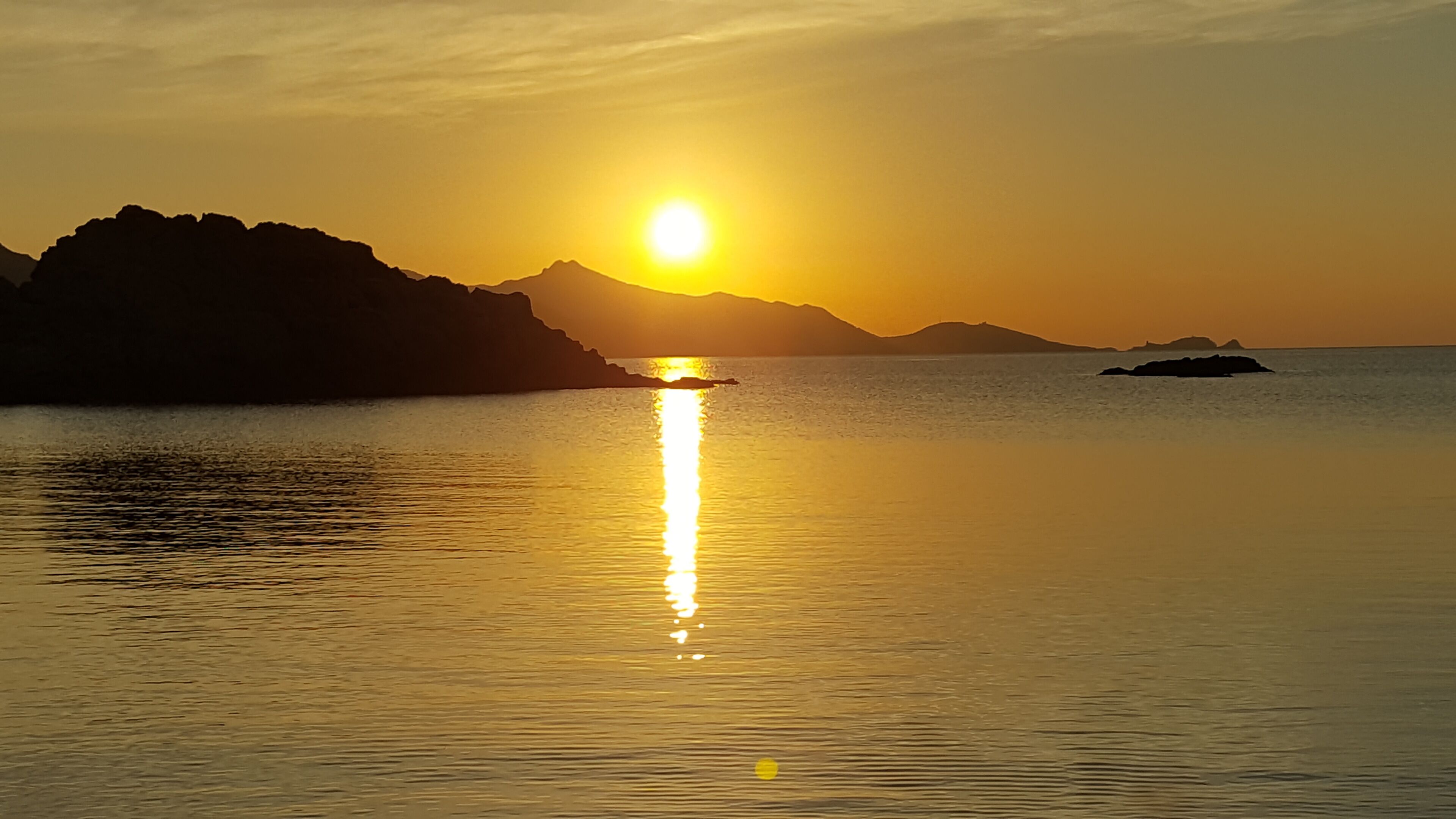 A sunset over calm waters with distant mountains.