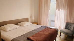 Una habitación de hotel con cama, una silla, una lámpara y un ventanal con cortinas.
