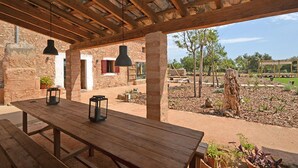 A rustic outdoor patio with a wooden table and hanging pendant lights, surrounded by stone walls and a garden. - Can Cortana - Charming country house with pool in Inca, Mallorca (Inca)