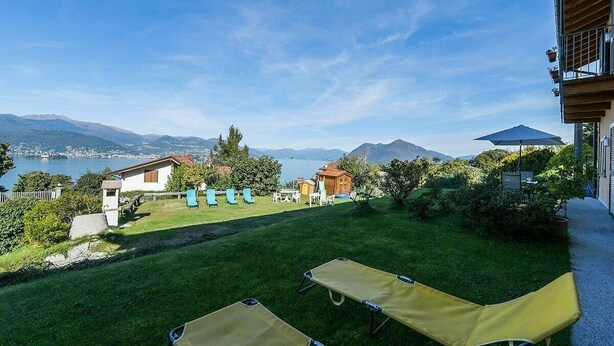A view of a hotel property with a grassy lawn, lounge chairs, and a scenic mountain backdrop. - Africa apartment over Stresa with lake view (Stresa)
