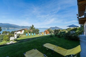 Vue d’un hôtel avec une pelouse verdoyante, des chaises longues et un paysage montagneux en toile de fond.