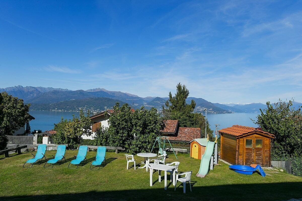 Un giardino con vista sulle montagne e su un lago, che include un'area giochi con scivoli e una piccola casetta di legno.