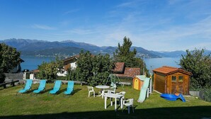 A backyard with a view of mountains and a lake, featuring a play area with slides and a small wooden cabin. - Africa apartment over Stresa with lake view (Stresa)