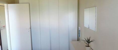 Ein Zimmer mit Schrank, einem kleinen Tisch mit Pflanze und einem Spiegel an der Wand.