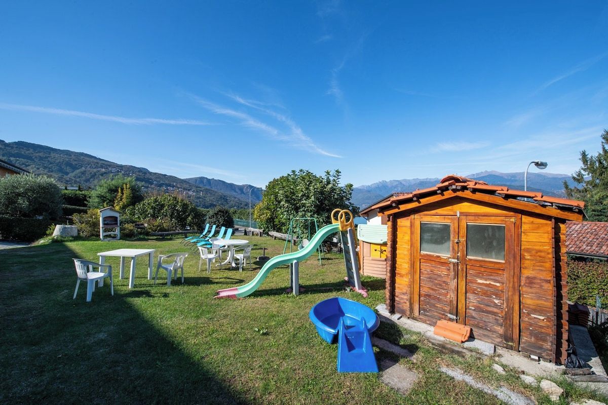 A playground with slides and tables, a small wooden building, and a mountainous backdrop.