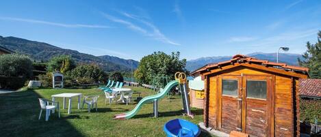 A playground with slides and tables, a small wooden building, and a mountainous backdrop.