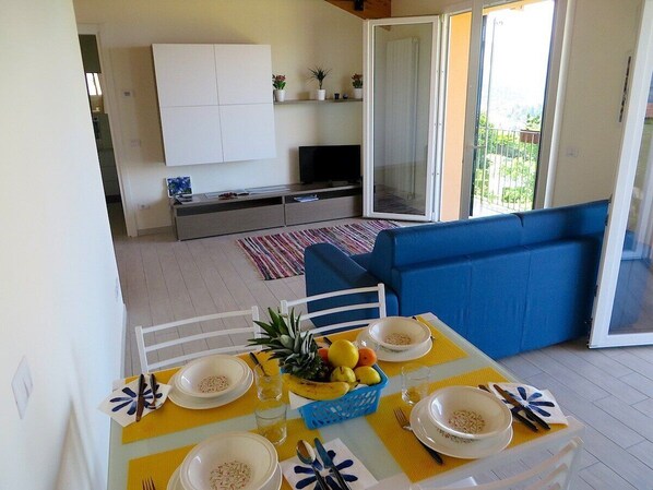 A dining area with a table set for two, a blue sofa, and a sliding glass door leading to a balcony.