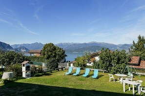 Vista de un paisaje montañoso con un lago, una zona de césped con mesas al aire libre y un pequeño edificio.