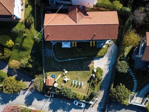 Vue aérienne d’une propriété résidentielle dotée d’un toit recouvert de tuiles rouges, d’une piscine et d’un jardin aménagé avec des chaises longues.