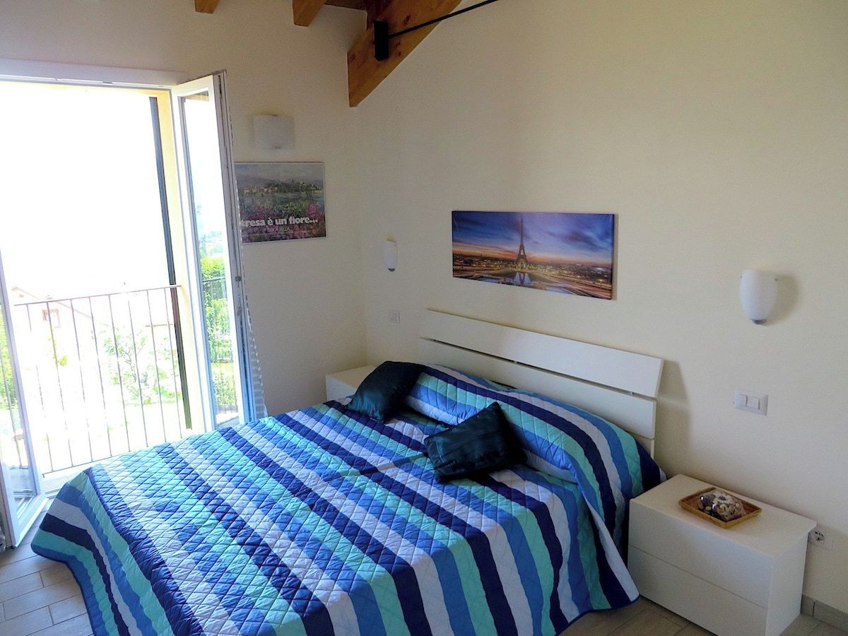 Un dormitorio con cama, mesita de noche, un cuadro en la pared y ventana.