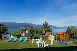 Un jardin avec vue sur les montagnes et un lac, comprenant un espace de jeux avec des toboggans et un petit chalet en bois.