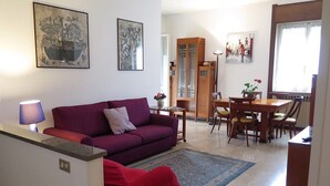 Un soggiorno con un divano viola, una poltrona rossa, un'area pranzo con tavolo e sedie in legno, e opere d'arte alle pareti.