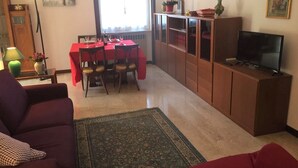 Un soggiorno con un divano rosso, un tavolo da pranzo con sedie, una TV su un mobile e una lampada da terra.