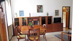Zona pranzo con tavolo e sedie in legno, una libreria e un televisore.