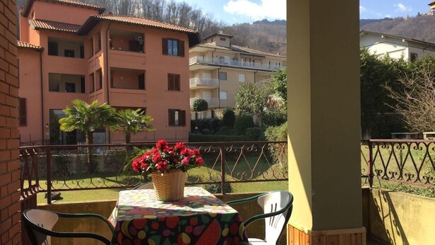 Un balcone con tavolo e sedie, un cesto di vimini con fiori e sullo sfondo edifici a più piani.