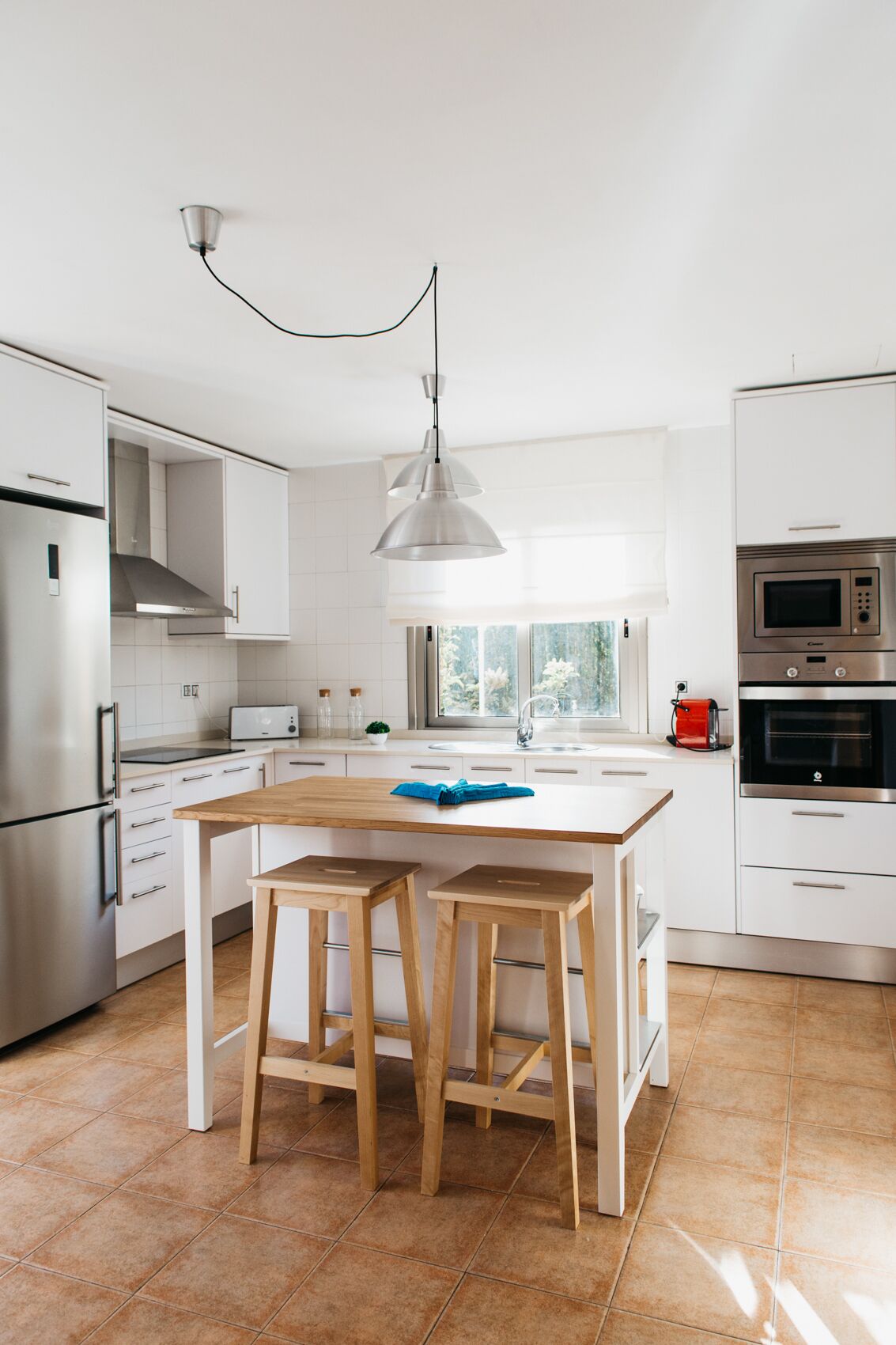 A modern kitchen with white cabinetry, stainless steel appliances, a wooden island with stools, and a pendant light.