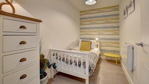 A bedroom with a bed, a bedside table, a lamp, a radiator, and a wall with a striped pattern.