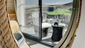 A round mirror with a rope frame reflecting a balcony with a view of the sea and distant land.