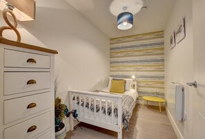 A bedroom with a bed, a bedside table, a lamp, a radiator, and a wall with a striped pattern.